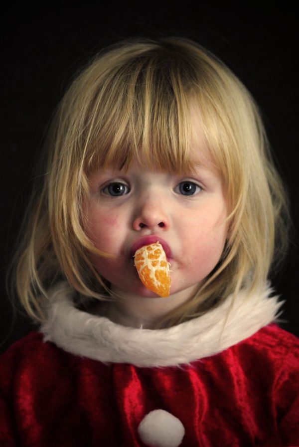 Ein kleines Weihnachtsmädchen mit einem Stück Mandarine im Mund